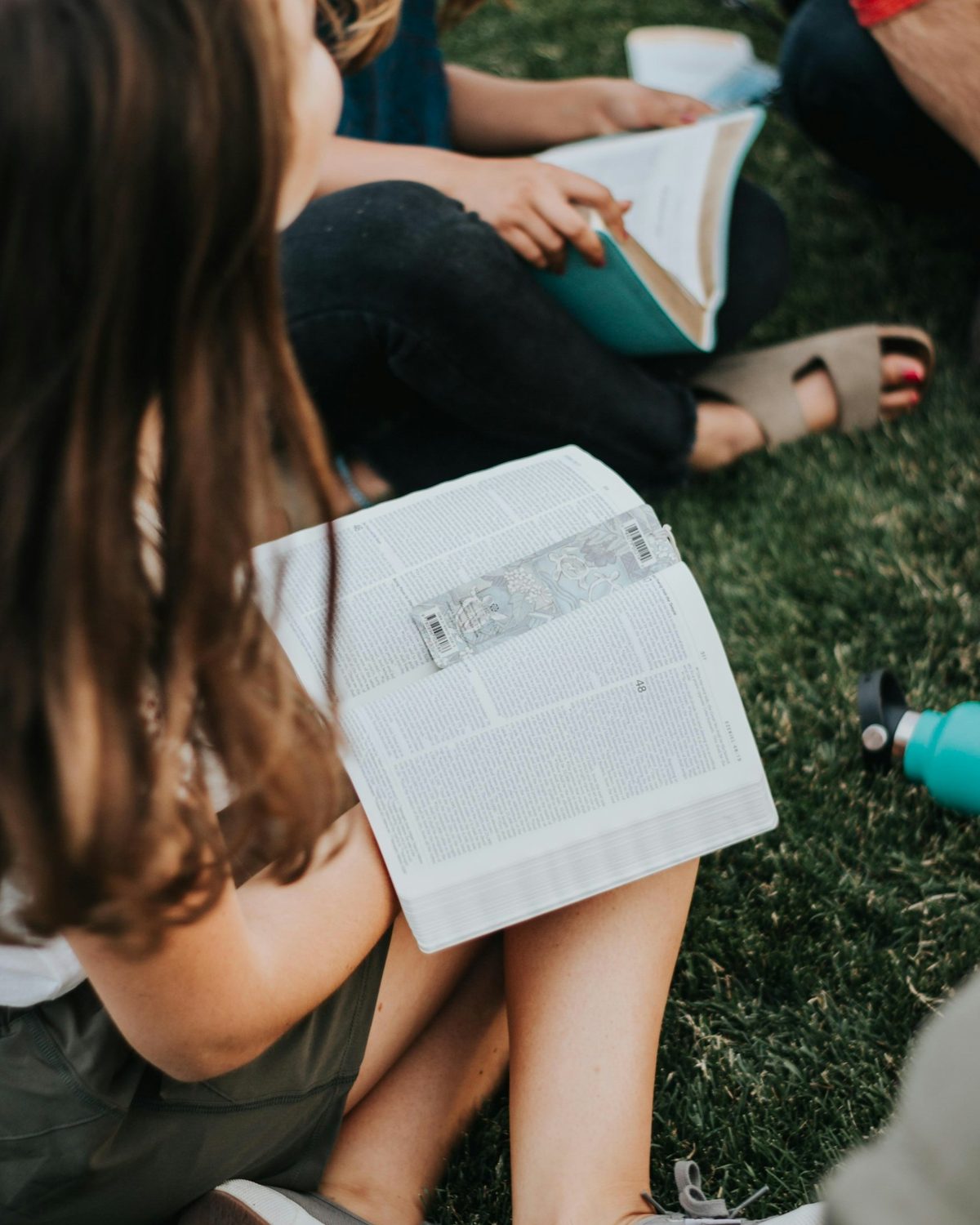 Friends sitting on the grass reading their Bibles together