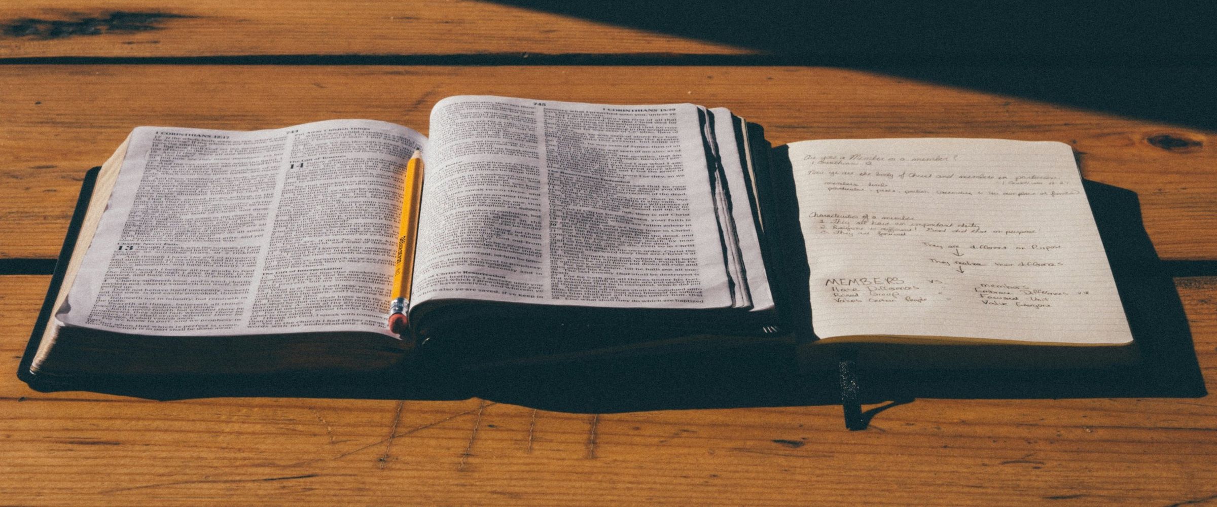 An open Bible, pencil and study notebook on a sunlit wooden table
