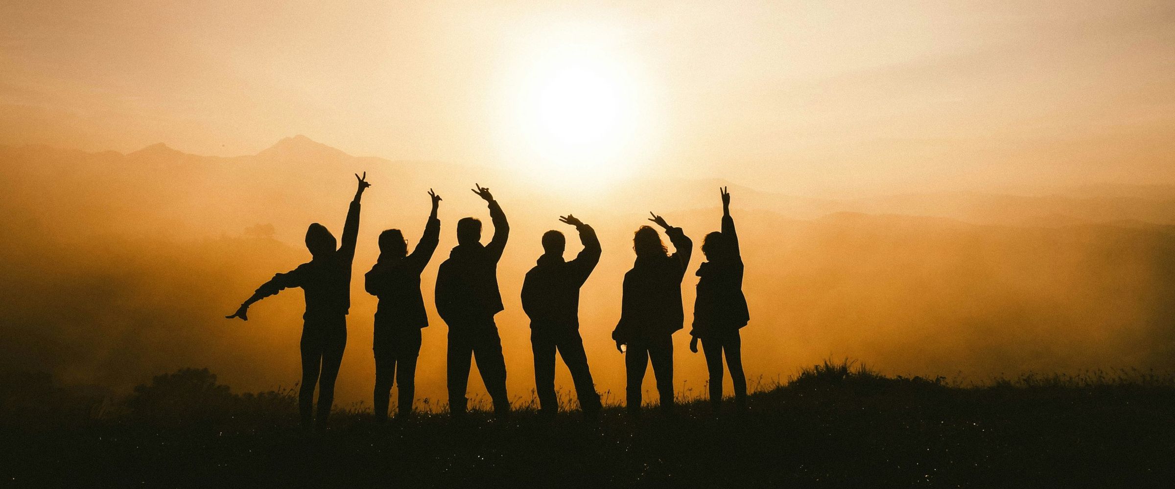 A group of friends waving at the sunset from a hilltop